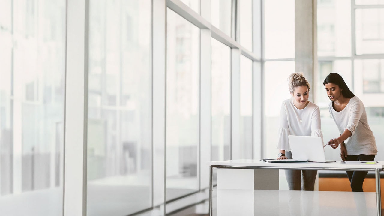 Two colleagues talking and looking at a laptop in an office